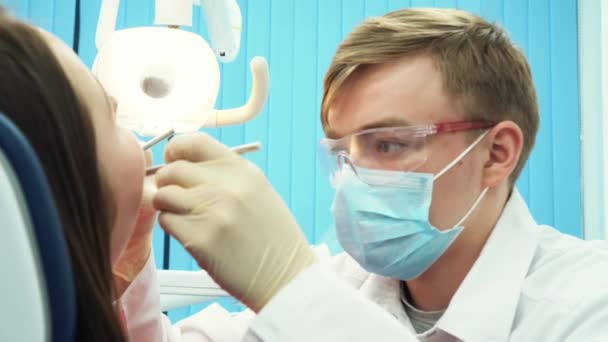 Primer plano del joven dentista que trata los dientes a una paciente joven en el consultorio dental. Cuidado dental . — Vídeos de Stock