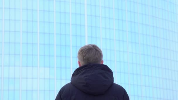 Achteraanzicht van de man die in het gebouw van glas. Media. Man staat en glazen gevel van moderne kantoorgebouw kijkt — Stockvideo