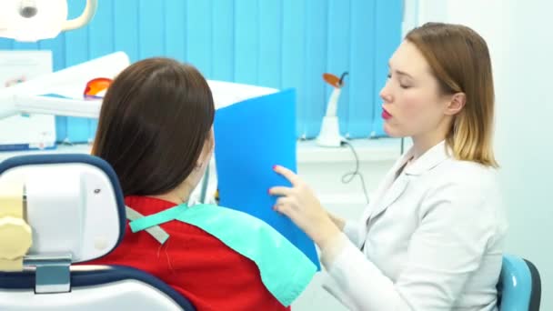 치과 상담에서 치료를 선택 하는 그녀의 손에 파란 폴더와 환자와 치과 의사 조 수의 클로즈업. 치과 치료. — 비디오