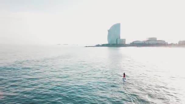 Luchtfoto van de jonge man zwemmen op paddle board in duidelijk turkoois zeewater tegen blauwe hemel. Voorraad. Resort seizoen. — Stockvideo