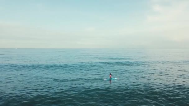 Aerial view of the young man swimming on paddle board in clear turquoise sea water against blue sky. Stock. Resort season. — Stock Video