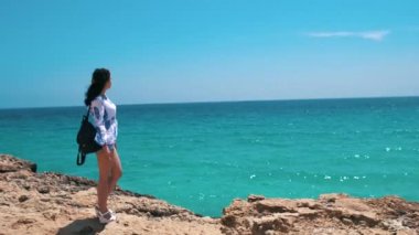 Genç kız bir uçurumun kenarında duruyor ve denizde görünüyor. Güzel kız deniz cliff bir manzaraya sahip. Kız uçurumun kenarına okyanus manzarası hoşlanır