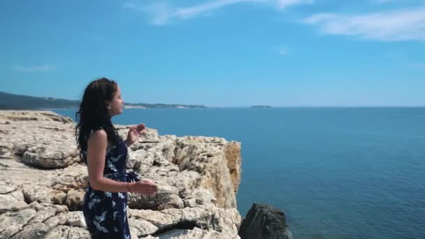 Jong meisje staat op de rand van een klif en kijkt naar de zee. Mooi meisje geniet van een uitzicht op de klif boven de zee. Meisje op de rand van de klif geniet van het uitzicht op de Oceaan — Stockvideo