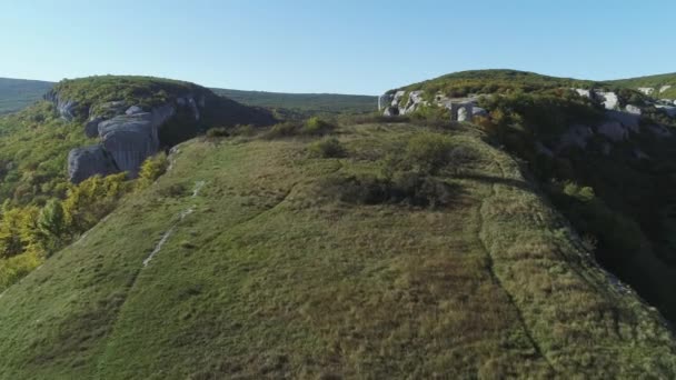 På toppen av klippan. Skott. Vackert landskap med enorma klippor, grönt gräs och stenar mot blå himmel — Stockvideo