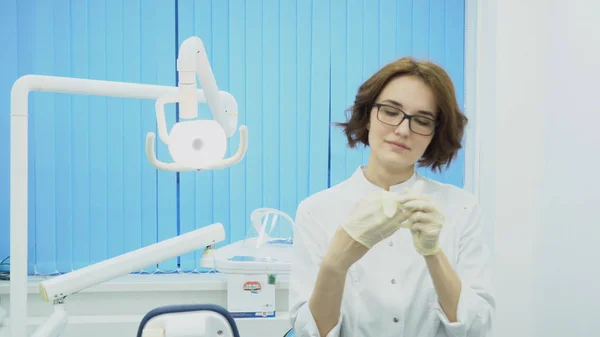 Vrouw tandarts legt op handschoenen in tandheelkundige kantoor. Media. Vrouw tandarts in uniform zet op de handschoenen wassen voordat de werkzaamheden aanvangen — Stockfoto