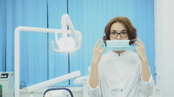 Vrouw tandarts draagt een masker in tandheelkundige kantoor. Media. Aantrekkelijke vrouw tandarts in masker en witte jas is klaar om te werken. Tandheelkundige concept — Stockfoto