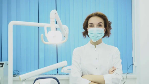 Vrouw tandarts draagt een masker in tandheelkundige kantoor. Media. Aantrekkelijke vrouw tandarts in masker en witte jas is klaar om te werken. Tandheelkundige concept — Stockfoto