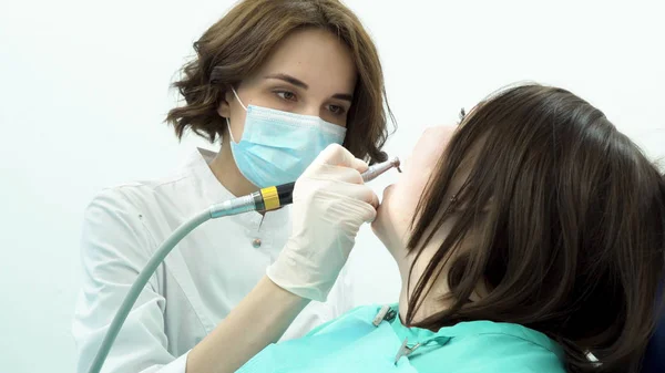 La dentista blanquea los dientes de la paciente. Medios. Odontóloga profesional limpia los dientes de las pacientes antes de blanquear con nuevos equipos estériles de estomatología —  Fotos de Stock