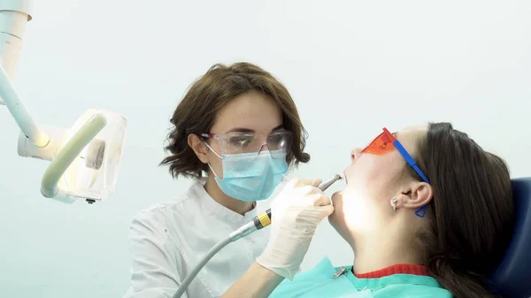 Mujer dentista pule los dientes de la paciente. Medios. Atractivo dentista pule sus dientes con cepillo antes del procedimiento de blanqueo con equipo profesional —  Fotos de Stock