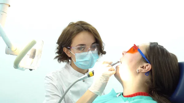 Mujer dentista pule los dientes de la paciente. Medios. Atractivo dentista pule sus dientes con cepillo antes del procedimiento de blanqueo con equipo profesional —  Fotos de Stock