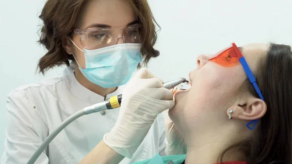 Vrouw tandarts polijst tanden van patiënt. Media. Aantrekkelijke tandarts poetsmiddelen haar tanden met de borstel voor het bleken van de procedure met professionele apparatuur — Stockfoto