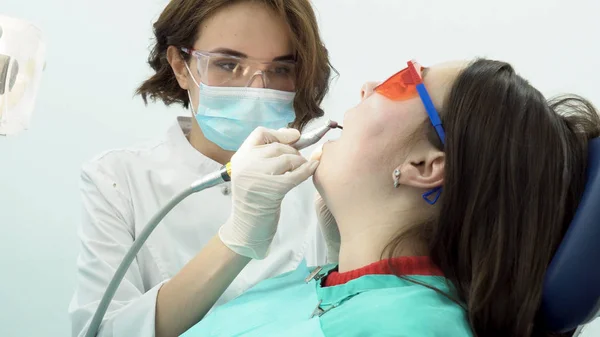 Vrouw tandarts polijst tanden van patiënt. Media. Aantrekkelijke tandarts poetsmiddelen haar tanden met de borstel voor het bleken van de procedure met professionele apparatuur — Stockfoto