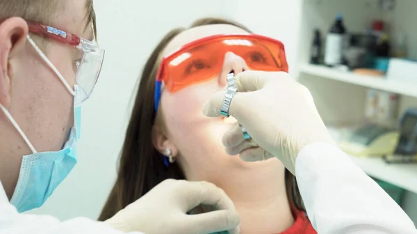 Close-up of dentist working with woman. Media. Dentist makes dental hygiene young woman. Dentist sticks his syringe into mouth of patient. Oral and dental treatment and care