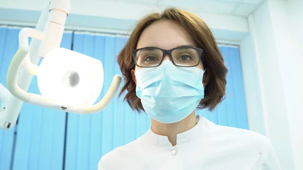Onderaanzicht van vrouwelijke tandarts. Media. Aantrekkelijke vrouw tandarts draaien op elektronische lamp onderzoekt de mondholte patiënten — Stockfoto