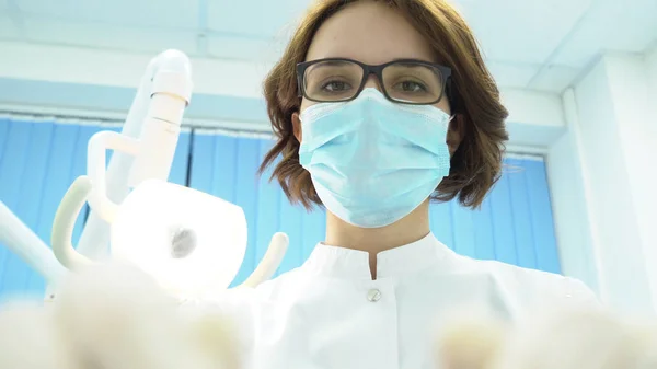 Spodní pohled na ženské zubaře. Média. Atraktivní žena zubař s nástroje v ruce léčí zuby na pozadí zubní elektronické svítilny — Stock fotografie