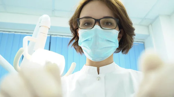 Vista inferiore del dentista femminile. I media. Attraente dentista donna con strumenti in mano tratta i denti sullo sfondo della lampada elettronica dentale — Foto Stock