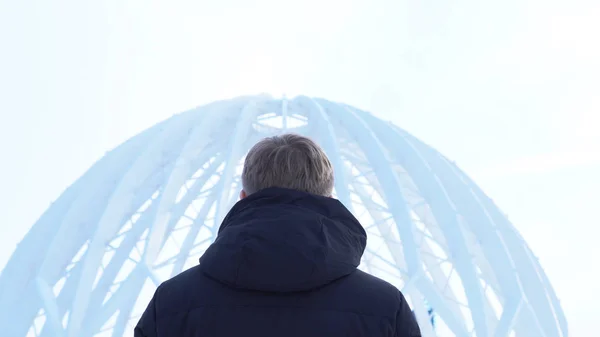 Back view of man looking at dome building. Media. View from back of man considering architectural structure of open dome against sky