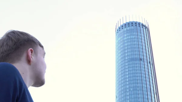 Visão traseira do homem olhando para o edifício de vidro. Mídia. Homem fica e olha para fachada de vidro do edifício de escritórios moderno — Fotografia de Stock