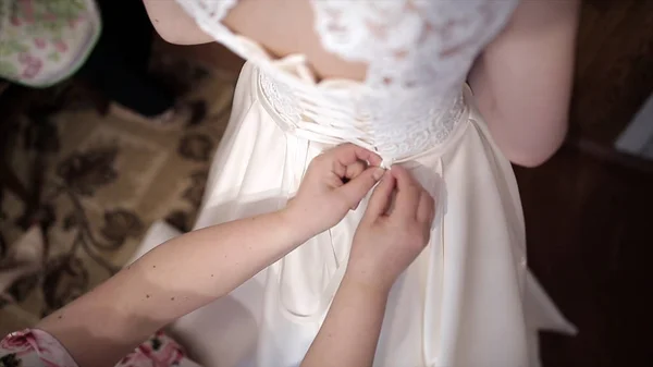 Madre ayuda a la novia a ponerse un vestido de novia. Acciones. Las manos atan el corsé del vestido de boda — Foto de Stock