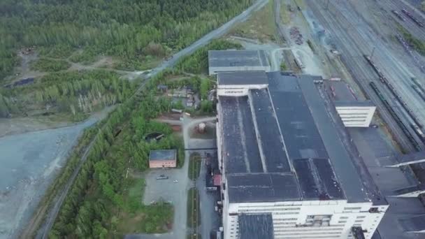 Letecký pohled na obrovské šedé průmyslové budovy blízko železnice a skládce, obklopen lesem. Průmyslová zóna shora.