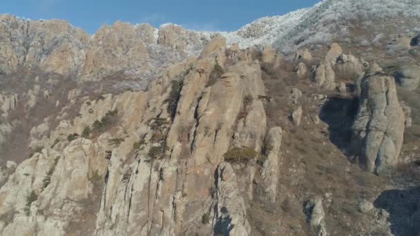 Aerial view of a huge boulders on a mountainside against the mountain top covered by snow and blue sky. Shot. Winter mountain landscape. — Stock Video