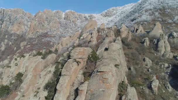 Luftaufnahme eines riesigen Felsbrockens an einem Berghang gegen die von Schnee und blauem Himmel bedeckte Bergspitze. Schuss. Winterliche Berglandschaft. — Stockvideo