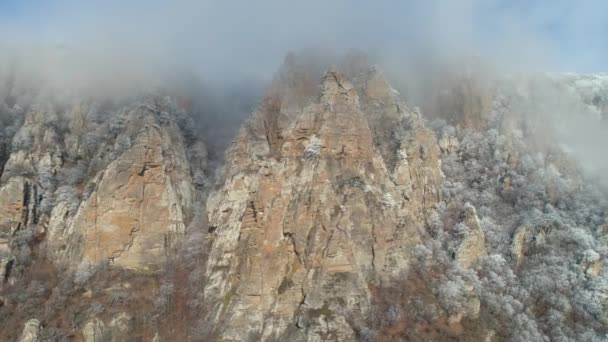 Enormes y viejos acantilados en una ladera cubierta de arbustos y árboles de coníferas congelados en nubes grises contra el cielo azul. Le dispararon. Hermosa vista . — Vídeo de stock