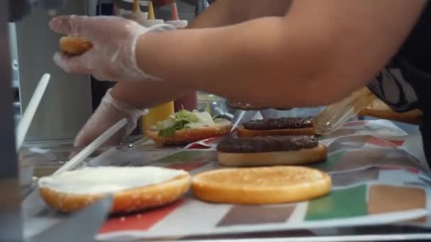 Primer plano de los trabajadores de McDonald cocinando hamburguesas clásicas con chuleta frita, queso y verduras, enfoque selectivo. Una trampa. Preparación de deliciosas hamburguesas . — Vídeos de Stock