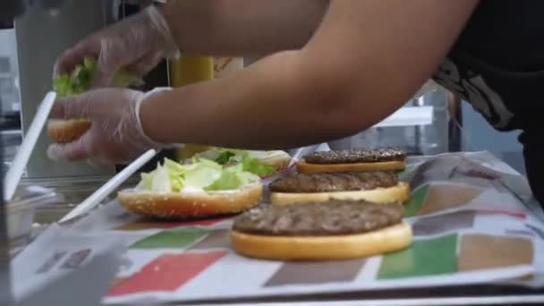 Primer plano sobre la preparación de hamburguesas clásicas. Una trampa. Chef agrega ensalada y tomates a la chuleta frita en un bollo de hamburguesa . — Vídeo de stock