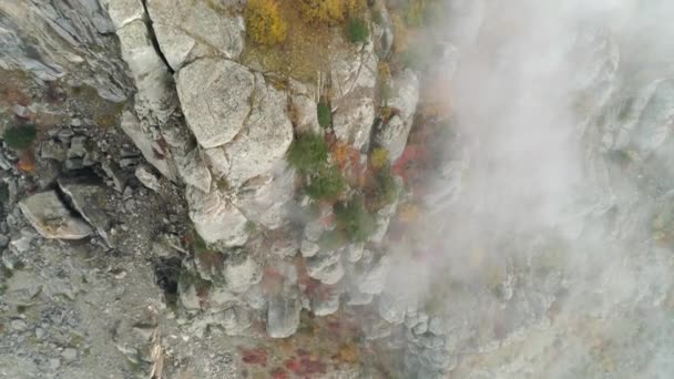 Vista aérea sobre la ladera rocosa de la montaña en nubes cubiertas de pequeños árboles con hojas verdes, amarillas y rojas. Le dispararon. Colorido paisaje de montaña — Vídeo de stock