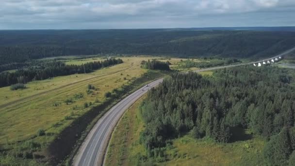 Flygfoto på körbanan mellan grön tät skog och fält med rörliga bilar. Klipp. Kör bil — Stockvideo