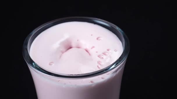 Närbild av färska strawberry milkshake och jordgubbe fallit i glaset. Ram. Svart bakgrund — Stockvideo