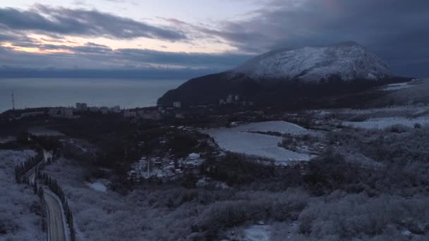 Vista aérea sobre la ciudad cubierta de nieve y la industria desde las montañas. Le dispararon. Desacelera desde un afloramiento rocoso para mostrar la industria, una pequeña ciudad y las montañas circundantes — Vídeos de Stock