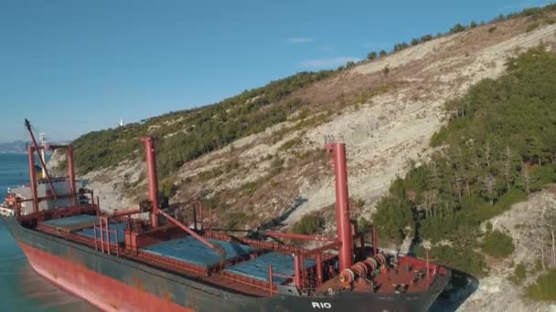 Vista aerea su una grande nave da carico vicino alla costa e alla collina con persone che camminano lungo. Gli hanno sparato. Trasporti marittimi — Video Stock