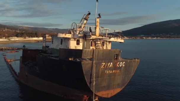 Close-up of abandoned rusty ship aground against beautiful sunset sky, mountains and coastline. Shot. Old seagoing vessel — Stock Video