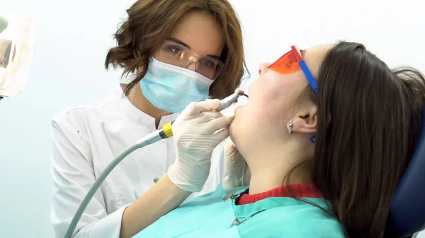 在牙医办公室进行体检时坐在牙科椅上的年轻女子。媒体。美丽的女牙医治疗病人牙齿的侧视图. — 图库照片