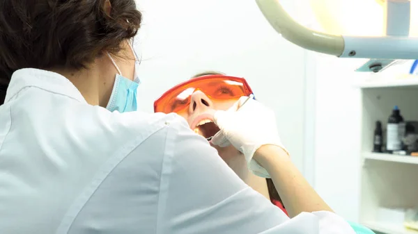 Afdeling Stomatologie arts vrouw tanden in tandheelkunde kliniek behandelen. Media. Vrouw liggend met geopende mond en vrouwelijke tandarts in wit uniform en handschoenen met behulp van instrumenten. — Stockfoto