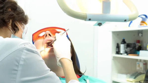 Afdeling Stomatologie arts vrouw tanden in tandheelkunde kliniek behandelen. Media. Vrouw liggend met geopende mond en vrouwelijke tandarts in wit uniform en handschoenen met behulp van instrumenten. — Stockfoto