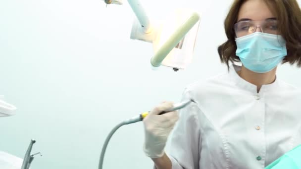 Mujer joven sentada en la silla dental en un examen médico en el consultorio del dentista. Medios. Vista lateral del hermoso dentista femenino que trata los dientes del paciente . — Vídeos de Stock