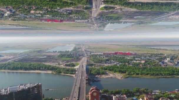 A légi felvétel a hídon átkelés széles folyó tükör horizon hatása, a város közelében. Média. Nyári táj, a zöld fák és egy híd, a kezdetektől téma folyóparton mezők. — Stock videók