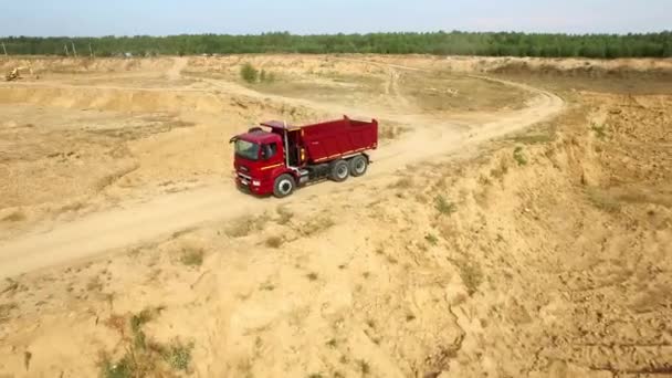 Camión volquete conduciendo por carretera rural. Escena. Vista superior de los paseos en camión, dejando columnas de polvo en el camino de tierra en el campo en el fondo de la carrera de la excavadora — Vídeo de stock