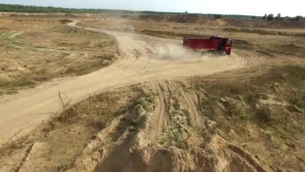 Paseos en camión por carretera polvorienta. Escena. Vista superior del camión volquete conduciendo en tierra de barro camino de hoyo abierto dejando rastro de polvo — Vídeo de stock