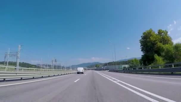 View from car on suburban highway. Scene. Highway at entrance to city with beautiful view of asphalt road, mountains on horizon and blue sky — Stock Video