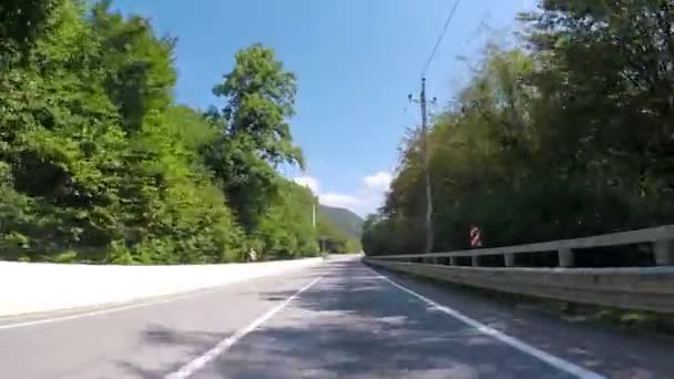 Paseos en coche por carretera de asfalto de montaña con bosque. Escena. Carretera de campo en zona montañosa con tráfico y hermoso paisaje con vegetación y cielo azul — Vídeo de stock