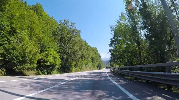 Passeios de carro na estrada de asfalto de montanha com floresta. Cena. Estrada do campo na área montanhosa com tráfego e bela paisagem com vegetação e céu azul — Fotografia de Stock