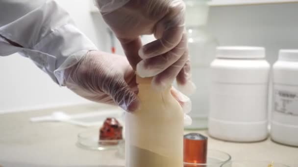 Somebodys のクローズ アップは、大きな白いボトルの背景にいくつかの白い粉末がボトルを開けて白手袋で手します。映像素材集。化学実験 — ストック動画