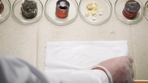 Primer plano de los científicos mano tomando uno de los minerales sobre la mesa y poniendo esto en un tejido blanco. Imágenes de archivo. Experimentos químicos — Vídeos de Stock