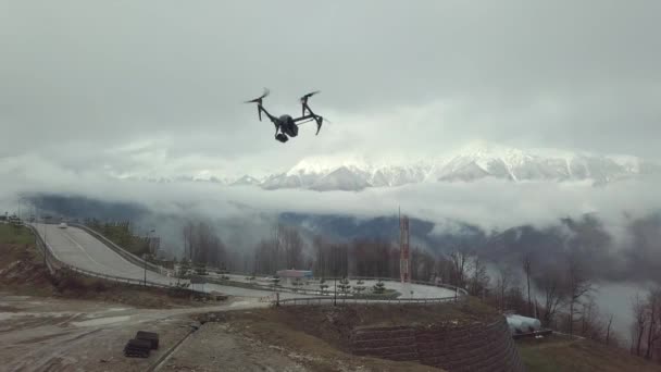 Nahaufnahme einer Quadrocopter-Drohne, die über die Straße fliegt, mit Bergen im weißen Nebel und Schnee im Hintergrund. Archivmaterial. Schießprozess — Stockvideo