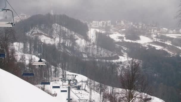 Nahaufnahme von Seilbahnkabinen in den Bergen gegen die schneebedeckten Hügel und Gebäude. Archivmaterial. Skigebiet — Stockvideo