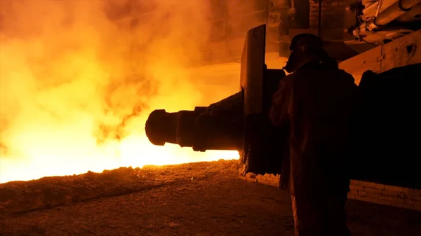 Steel worker near the molten metal flowing in the chute. Stock footage. Metallurgical equipment and technology of iron production. Blast furnace.